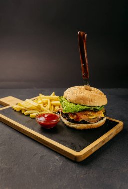 Klasik hamburger, taze marul ve domates yanında kızarmış patates ve ketçapla ahşap bir tahtanın üzerinde servis edilir. Yüksek kalite fotoğraf