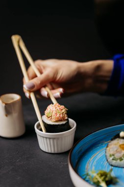 Hand dipping a sushi roll with crab topping into a small soy sauce dish. High quality photo clipart