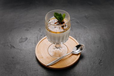 Elegant panna cotta dessert with passion fruit topping and mint in a glass on a wooden coaster. High quality photo clipart