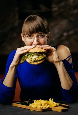 Woman enjoying a big bite of a gourmet burger with fresh greens, savoring each delicious flavor. High quality photo clipart