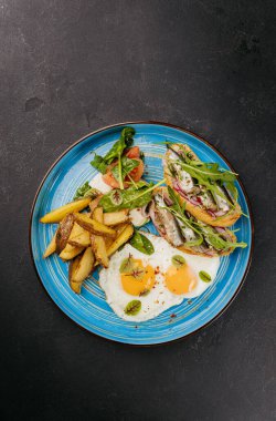 Kızarmış yumurtalı kahvaltı tabağı, kızarmış patates, taze salata ve mavi tabakta sardalya tostu. Yüksek kalite fotoğraf