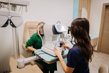 Optimetrist modern bir klinik ortamında gelişmiş ekipmanlarla göz testi yapıyor. Yüksek kalite fotoğraf