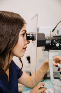 Klinikte modern bir yarık lambasıyla detaylı bir göz muayenesi yapan bir optometriste yaklaş. Yüksek kalite fotoğraf