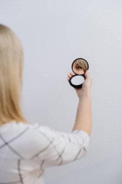 Reflection of a womans eye in a handheld compact mirror against a minimal background. High quality photo clipart