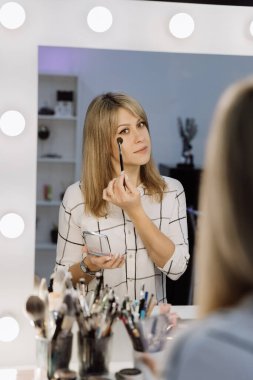 Parlak stüdyo ışıkları olan profesyonel bir aynanın önünde makyaj yapan zarif bir kadın. Yüksek kalite fotoğraf