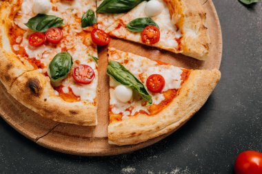 Fesleğenli taze dilimlenmiş Margherita pizza, mozzarella ve kırsal bir tabakta vişneli domates. Yüksek kalite fotoğraf