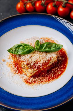 Taze fesleğenli İtalyan lazanyası ve canlı mavi bir tabakta parmesan, zamansız klasik bir yemek. Yüksek kalite fotoğraf