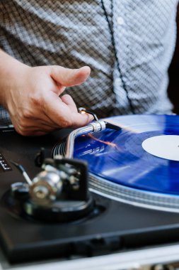 DJ turntable üzerinde mavi vinil plak çeviriyor, bir etkinlikte retro müzik titreşimleri yaratıyor. Yüksek kalite fotoğraf