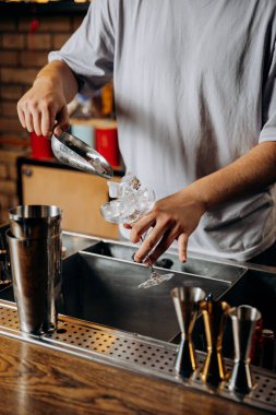 Barmen kokteyl bardağına buz ekliyor, modern bir bar ortamında ferahlatıcı bir içecek hazırlıyor. Yüksek kalite fotoğraf