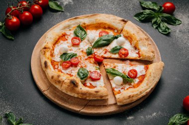 Fesleğenli taze dilimlenmiş Margherita pizza, mozzarella ve kırsal bir tabakta vişneli domates. Yüksek kalite fotoğraf