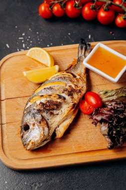Taze salata, limon dilimleri ve ahşap tabakta sosla servis edilen ızgara balık. Yüksek kalite fotoğraf