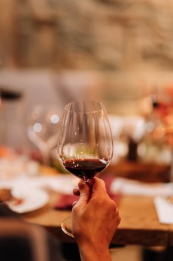 Hand holding a glass of red wine at a cozy dinner gathering with candles and elegant table decor. High quality photo clipart