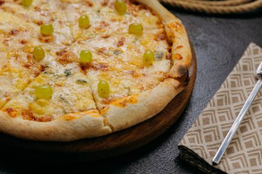 Dört peynirli yeşil üzümlü gurme pizza, şık bir restoran ortamında ahşap tahtada servis ediliyor. Yüksek kalite fotoğraf