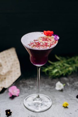 Elegant purple cocktail in a martini glass, garnished with dried lime, petals, and edible flowers. High quality photo clipart