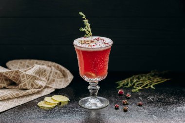 Limonlu, otlu ve çiçekli zarif kırmızı kokteyl. Koyu yüzeyde klasik camla servis ediliyor. Yüksek kalite fotoğraf
