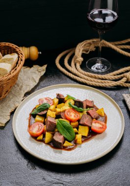 Kızarmış patatesli gurme biftek küpleri, kiraz domatesleri ve bol soslu ıspanak ve şarap. Yüksek kalite fotoğraf