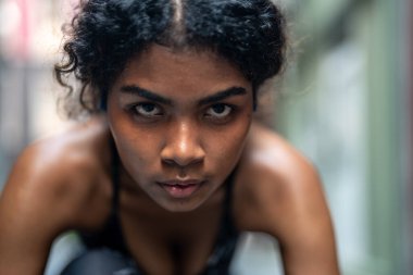 Güçlü atletik Afrikalı kadın koşucunun yakın plan yüzü. Gözü morarmış bir kadın konsantre oluyor. Spor kıyafetlerini giyerek şehrin arka planında koşmak. Spor ve spor motivasyonu. Çalıştırıcı kavramı.