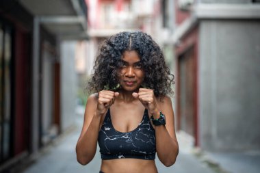 Çekici ve güçlü Afrikalı kadın açık hava sporlarından önce geriniyor. Spor konsepti. Sağlıklı bir yaşam tarzı. Kadın havadaki boksla ısınıyor..