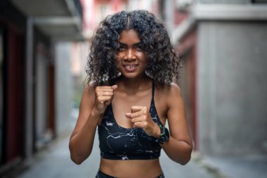 Çekici ve güçlü Afrikalı kadın açık hava sporlarından önce geriniyor. Spor konsepti. Sağlıklı bir yaşam tarzı. Kadın havadaki boksla ısınıyor..