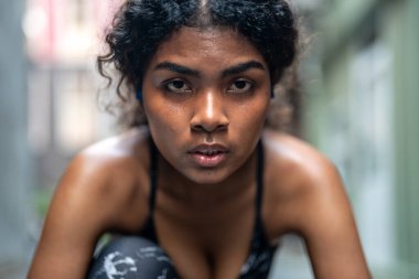 Güçlü atletik Afrikalı kadın koşucunun yakın plan yüzü. Gözü morarmış bir kadın konsantre oluyor. Spor kıyafetlerini giyerek şehrin arka planında koşmak. Spor ve spor motivasyonu. Çalıştırıcı kavramı.