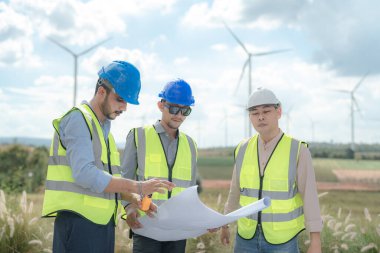 Saha görevinde çalışan Asyalı mühendis. İşçiler inşaat alanının etrafındaki inşaat ve makineleri kontrol ediyorlar. Temiz enerji ve çevresel sürdürülebilir elektrik için rüzgar türbini.