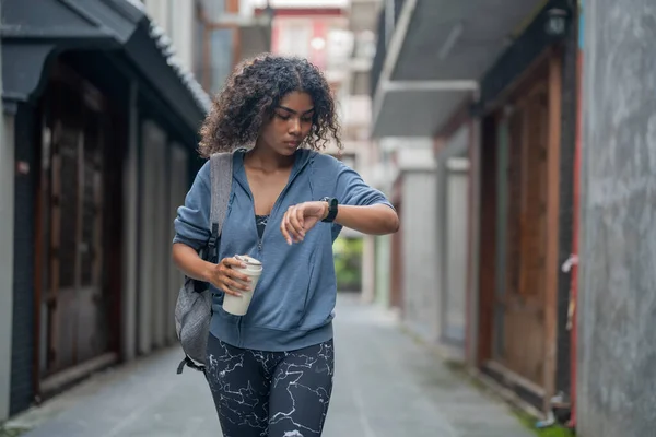 African woman sport healthy fit and firm slim drink water from cup on the hand. fitness girl wearing sportswear and jacket walking at city and town. Fitness and sport motivation.