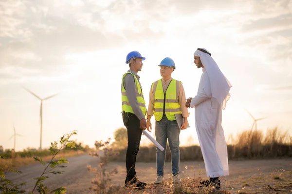 Asian Engineers and Arab businessman checking and inspecting on construction with sunset sky. people operation. Wind turbine for electrical of clean energy and environment. Industrial of sustainable.