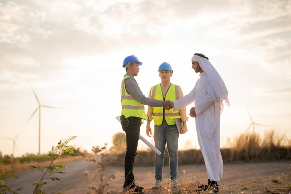 Asian Engineers and Arab businessman checking and inspecting on construction with sunset sky. people operation. Wind turbine for electrical of clean energy and environment. Industrial of sustainable.