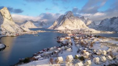 Norveç Lofoten Adası 'nın havadan görünüşü. Güneşin doğduğu kış mevsimi Reine balıkçı köyünün karlı dağ zirvesi suyu yansıtıyor. Norveç ve kırmızı rorbu evleri. Kışın yağan karla.