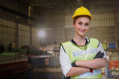Elle çalışan kadın işçinin portresi, ağır sanayi fabrikası için ön makinede çalışan süit elbise ve kaskla ayakta duruyor. Üretim için çelik metal levha fabrikası.