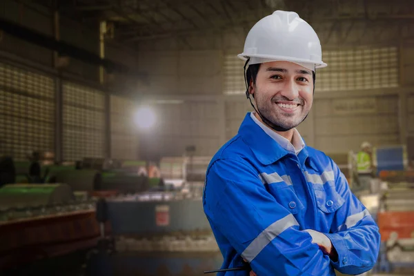 Portrait of manual man worker is standing with confident with working suite dress and safety helmet in front machine for heavy industry factory. Steel metal sheet plant for production.
