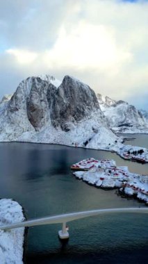 Norveç Lofoten Adası 'nın havadan görünüşü. Güneşin doğduğu kış mevsimi Reine balıkçı köyünün karlı dağ zirvesi suyu yansıtıyor. Norveç ve kırmızı rorbu evleri. Kışın yağan karla. 
