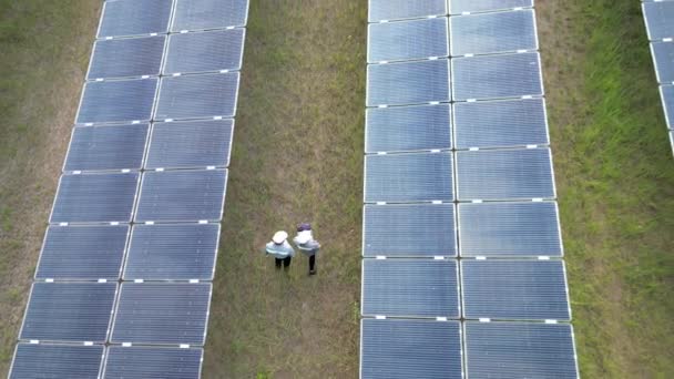 エンジニアはソーラーパネルをチェックし 太陽光発電所を歩く 太陽光パネルフィールド上のドローン飛行再生可能な緑の代替エネルギー — ストック動画