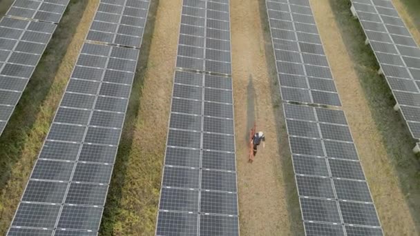 太陽光発電所をチェックするために太陽光発電所を歩く労働者のトップビュー 太陽光パネルフィールド上のドローン飛行再生可能な緑の代替エネルギー — ストック動画