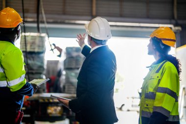 Kıdemli müdür kadrolu mühendis kadın ve Afrikalı adamla birlikte denetleme yapıyor. Fabrika binasının inşaat yapısını kontrol ediyorlar. Çelik çatı yapısı ve makine kurulumu olan depo.