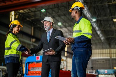 Kıdemli müdür kadrolu mühendis kadın ve Afrikalı adamla birlikte denetleme yapıyor. Fabrika binasının inşaat yapısını kontrol ediyorlar. Çelik çatı yapısı ve makine kurulumu olan depo.