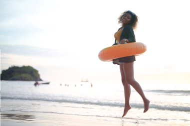 Seksi Asyalı Afrikalı kadın sahilde durup dinleniyor. Deniz ve sahilde yaz mevsimi. Tropik plajda sarı yüzme ringi oynayan kadın..