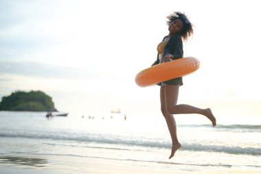 Seksi Asyalı Afrikalı kadın sahilde durup dinleniyor. Deniz ve sahilde yaz mevsimi. Tropik plajda sarı yüzme ringi oynayan kadın..