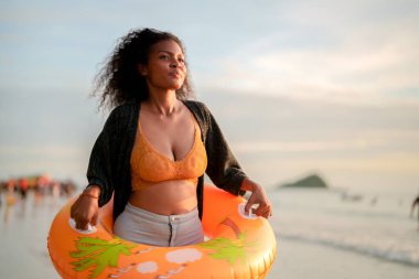 Seksi Asyalı Afrikalı kadın sahilde durup dinleniyor. Deniz ve sahilde yaz mevsimi. Tropik plajda sarı yüzme ringi oynayan kadın..