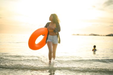 Seksi Asyalı Afrikalı kadın sahilde durup dinleniyor. Deniz ve sahilde yaz mevsimi. Tropik plajda sarı yüzme ringi oynayan kadın..