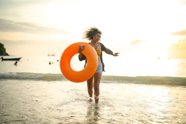 Seksi Asyalı Afrikalı kadın sahilde durup dinleniyor. Deniz ve sahilde yaz mevsimi. Tropik plajda sarı yüzme ringi oynayan kadın..