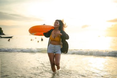 Seksi Asyalı Afrikalı kadın sahilde durup dinleniyor. Deniz ve sahilde yaz mevsimi. Tropik plajda sarı yüzme ringi oynayan kadın..