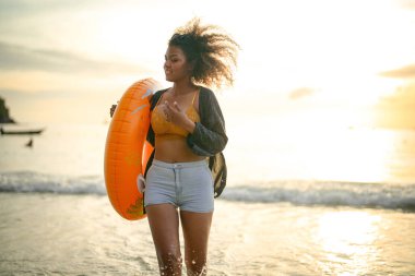 Seksi Asyalı Afrikalı kadın sahilde durup dinleniyor. Deniz ve sahilde yaz mevsimi. Tropik plajda sarı yüzme ringi oynayan kadın..