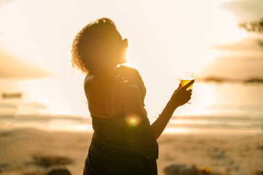 Afrikalı bir kadın tropik plajda mahsur kaldığında kokteyl suyu içiyor. Sarı bikini giyen ve doğanın güzelliğini ürperten genç bir gezgin. Seyahat ve seyahat kavramı. 