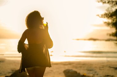 Afrikalı bir kadın tropik plajda mahsur kaldığında kokteyl suyu içiyor. Sarı bikini giyen ve doğanın güzelliğini ürperten genç bir gezgin. Seyahat ve seyahat kavramı. 