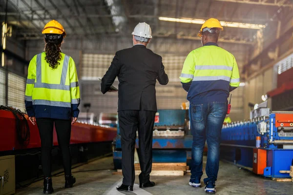 スタッフエンジニアの女性とアフリカ人男性と一緒に歩くシニアボスマネージャーの後ろ 鉄屋根構造と機械設置の倉庫 — ストック写真