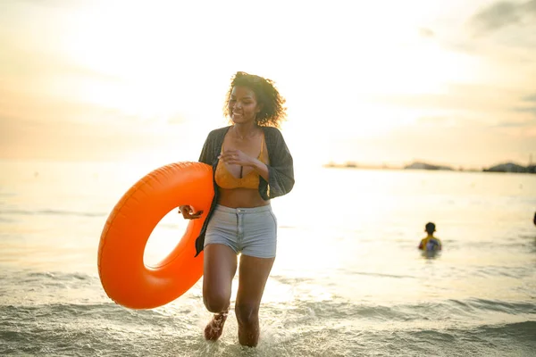 肖像セクシーなアジア系アフリカ人女性が立っていて ビーチでリラックスしています 海とビーチでの夏時間 熱帯のビーチで黄色いスイムリングをしている女性は — ストック写真