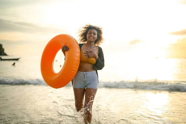 肖像セクシーなアジア系アフリカ人女性が立っていて ビーチでリラックスしています 海とビーチでの夏時間 熱帯のビーチで黄色いスイムリングをしている女性は — ストック写真