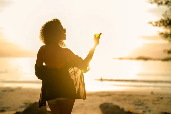 stock image African woman drinking cocktail juice when stranding at tropical beach. Young traveler wearing yellow bikini and chilling out the beauty of the Nature. Wanderlust and travel concept. 