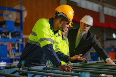 Kıdemli müdür kadrolu mühendis kadın ve Afrikalı adamla birlikte denetleme yapıyor. Fabrika binasının inşaat yapısını kontrol ediyorlar. Çelik çatı yapısı ve makine kurulumu olan depo.